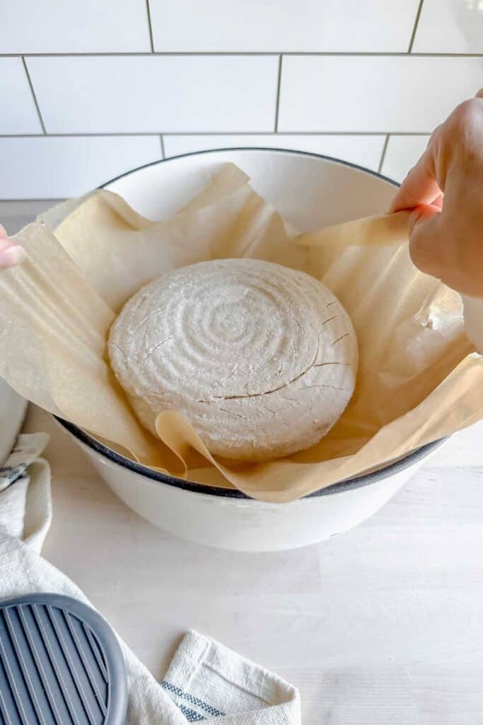 lowering a loaf of gluten free sourdough on parchment paper into dutchoven