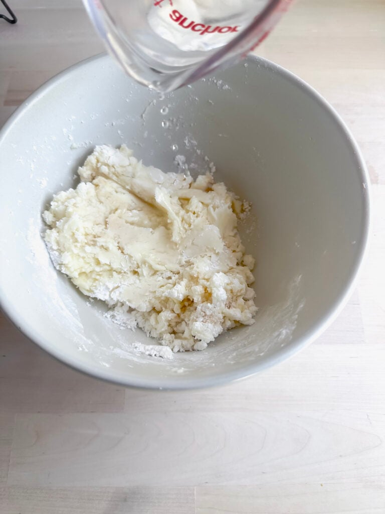 adding hot water to butter and powdered sugar mixture