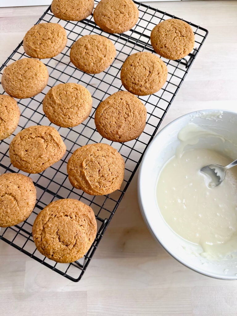 cooling rack lined with pumpkin cookies and a white bowl of frosting