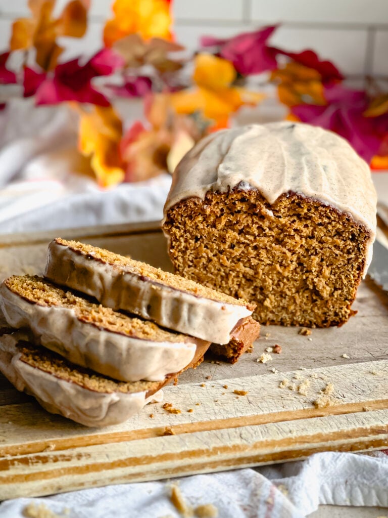 partially sliced gluten free pumpkin bread loaf on cutting board with frosting