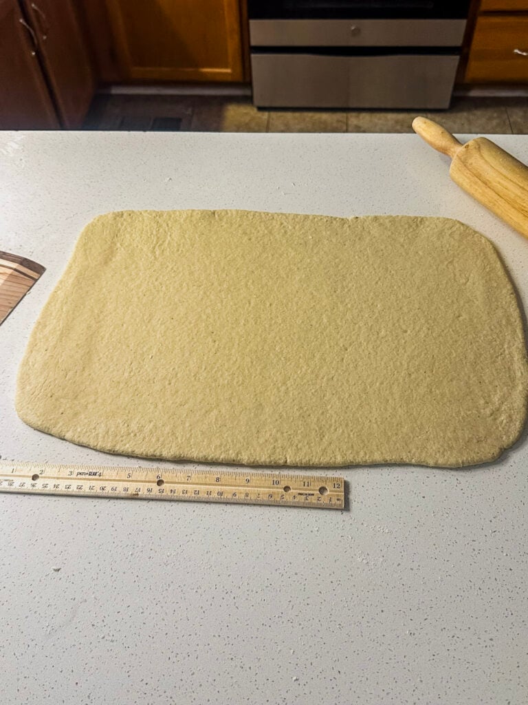 gf sourdough cinnamon roll dough rolled out in a rectangle on white counter top with a ruler near by