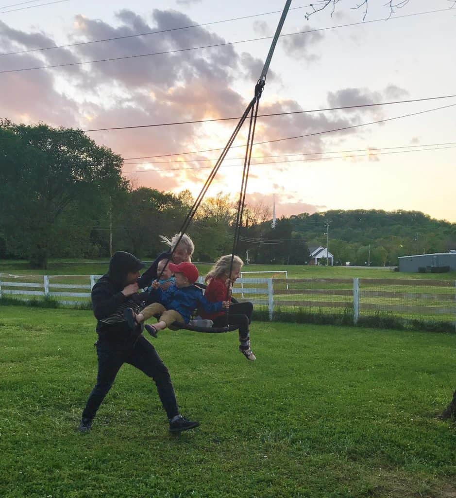 Dad pushing his 4 children on a large swing with a beautiful sunset in background