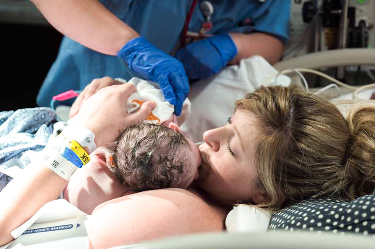 Mother kissing new born baby on hospital bed