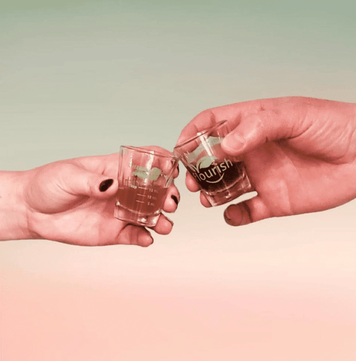 two hands holding liquid living probiotics in shot glasses