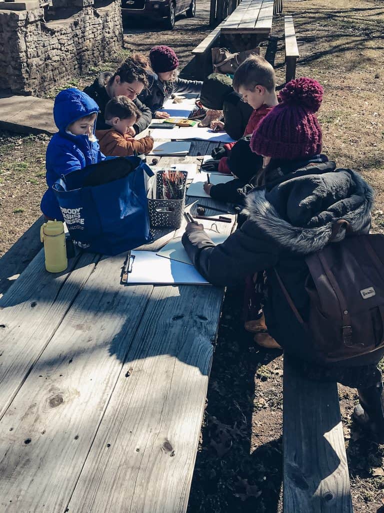 Nature study taking place at picnic tables with people wearing winter clothing