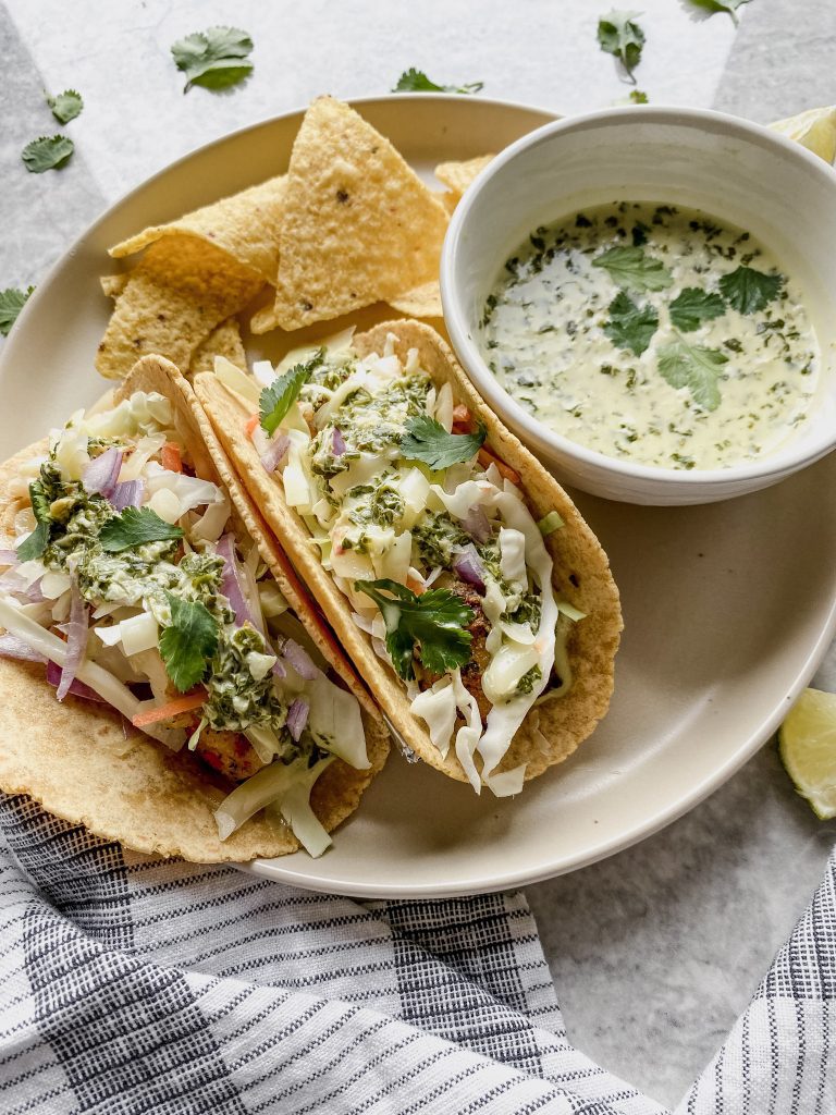 two fish tacos with cilantro lime crema like Costco and a bowl of sauce near by it 