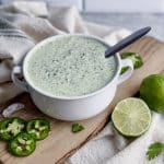 a bowl of cilantro lime crema sauce sits on a cutting board