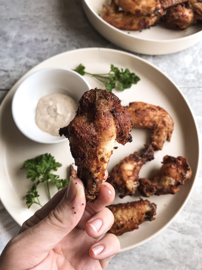 hand holding a chicken wing over a plate of wings on counter 