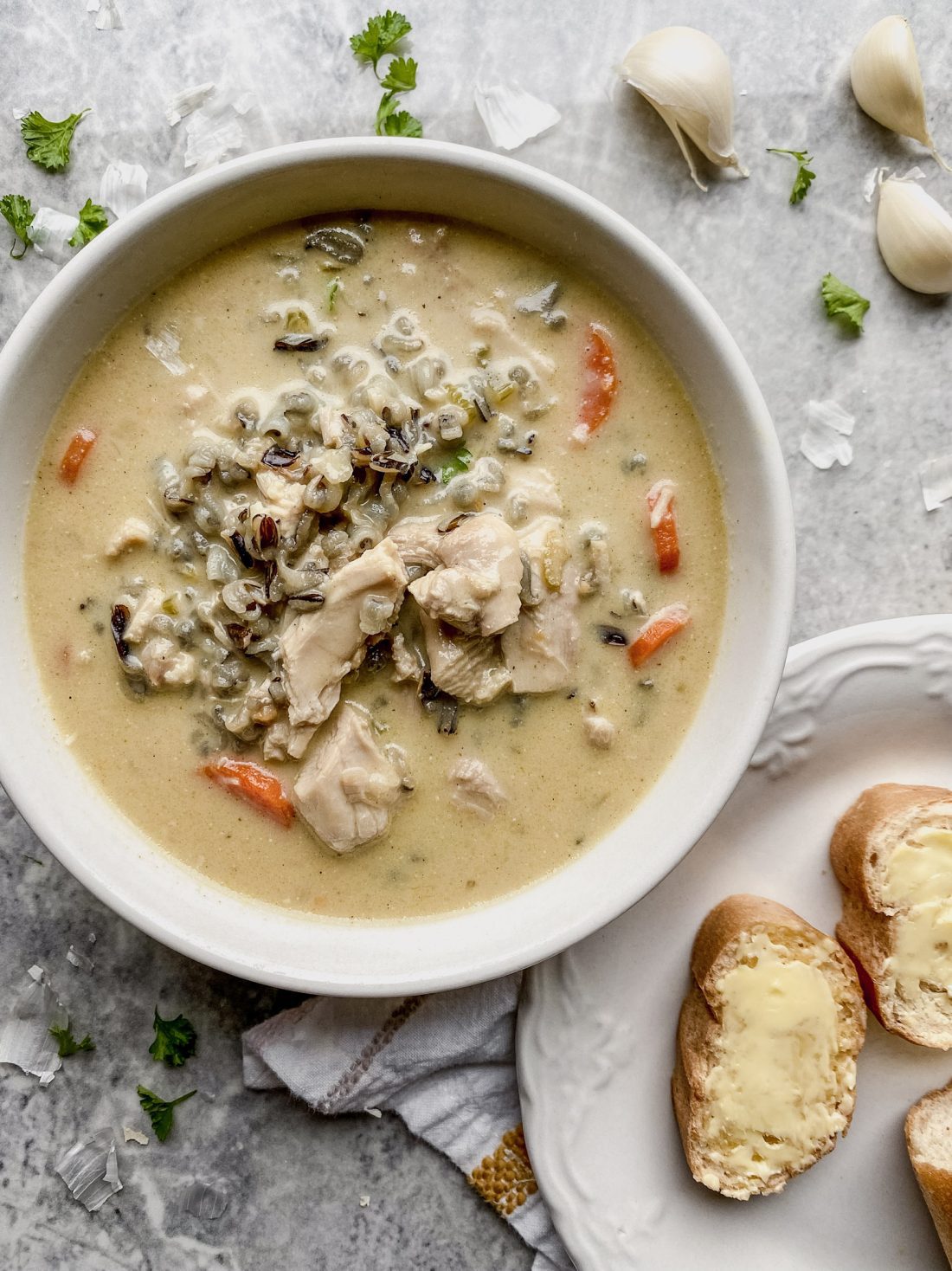 bowl of gluten free chicken wild rice soup on counter with bread and garlic cloves