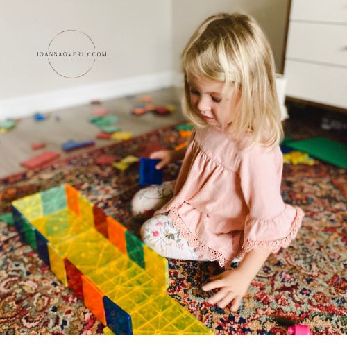 young girl in a pink shirt plays with magnet toys on a red rug