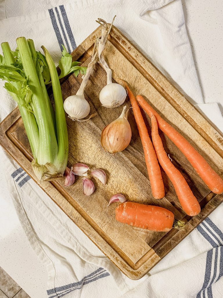 ingredients including celery, onion, carrots and garlic atop a wooden cutting board