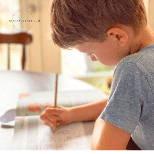 a boy in a blue shirt sits at the dining room table doing math lessons