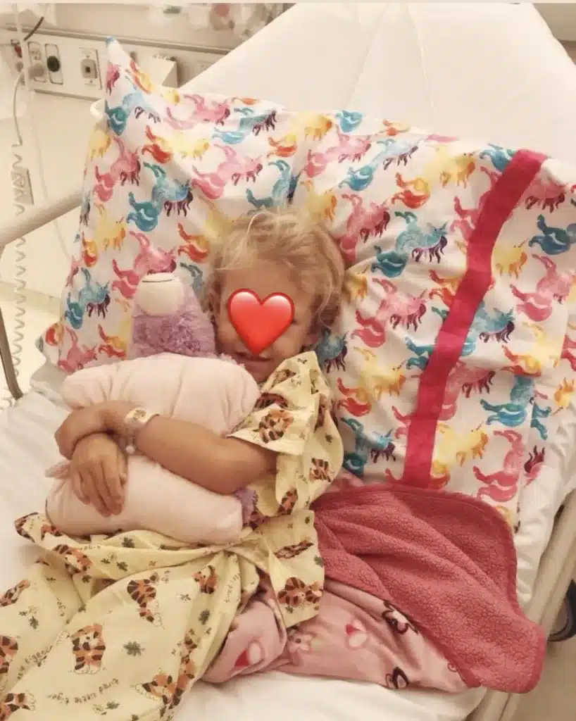 girl sitting on hospital bed with a stuffed animal in her arms