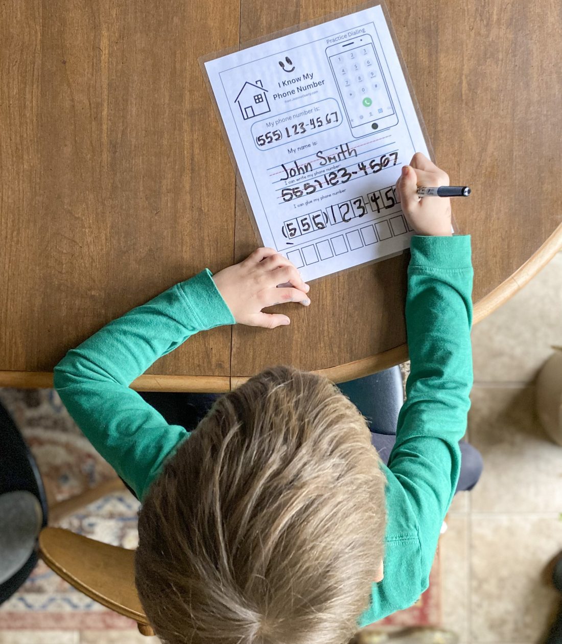 young boy sitting at table working on a phone number and address worksheet with expo marker