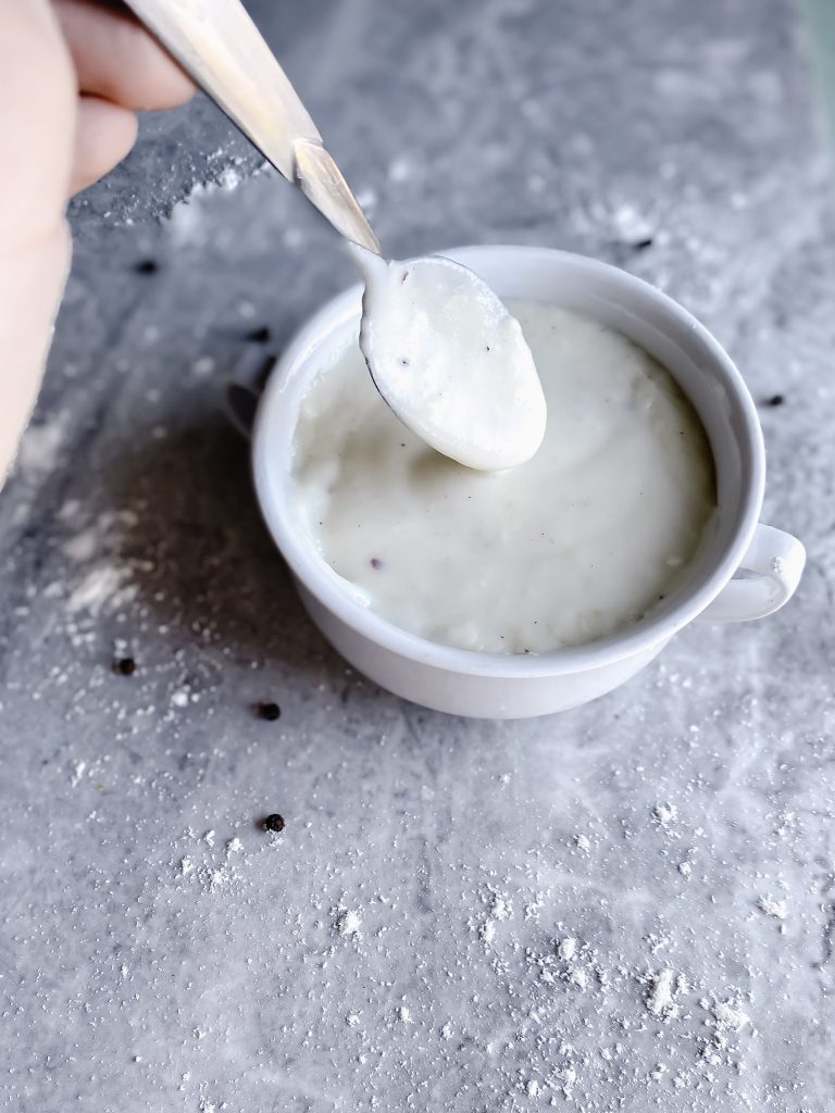 bowl of gluten free white sauce on gray counter with a spoon dripping with sauce