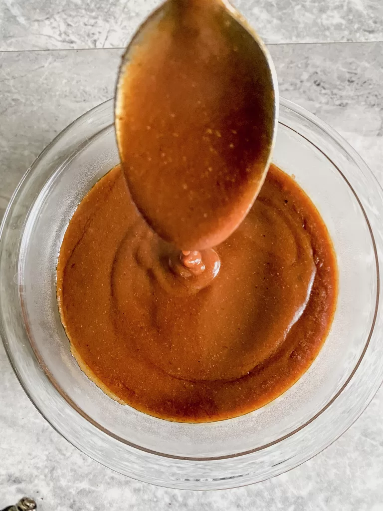 bowl of gluten free enchilada sauce with a spoon drizzling the sauce down into the bowl