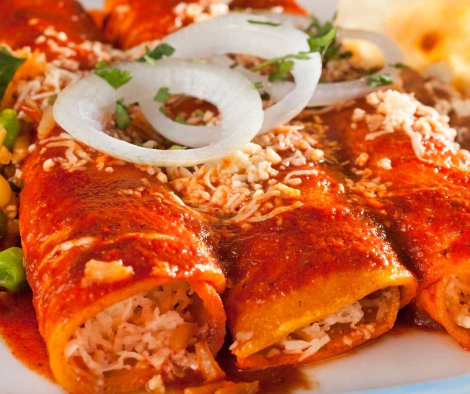 a plate of red enchiladas with onions on top and Spanish rice near by