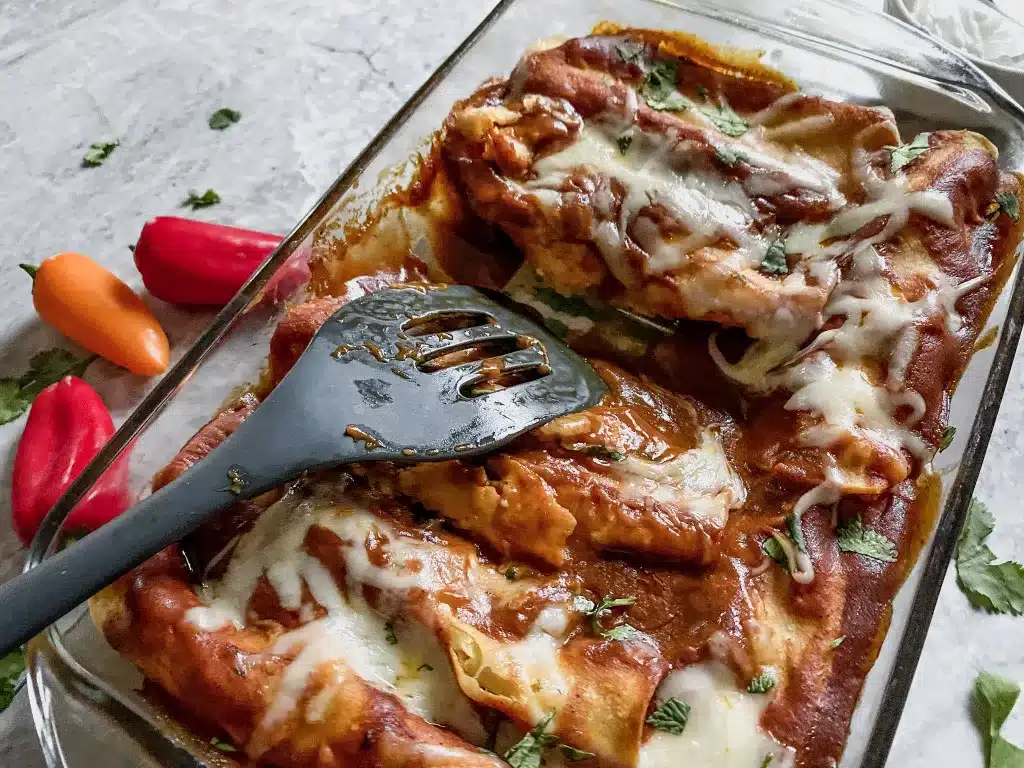 glass pan with gluten free chicken and cheese enchiladas and a spatula