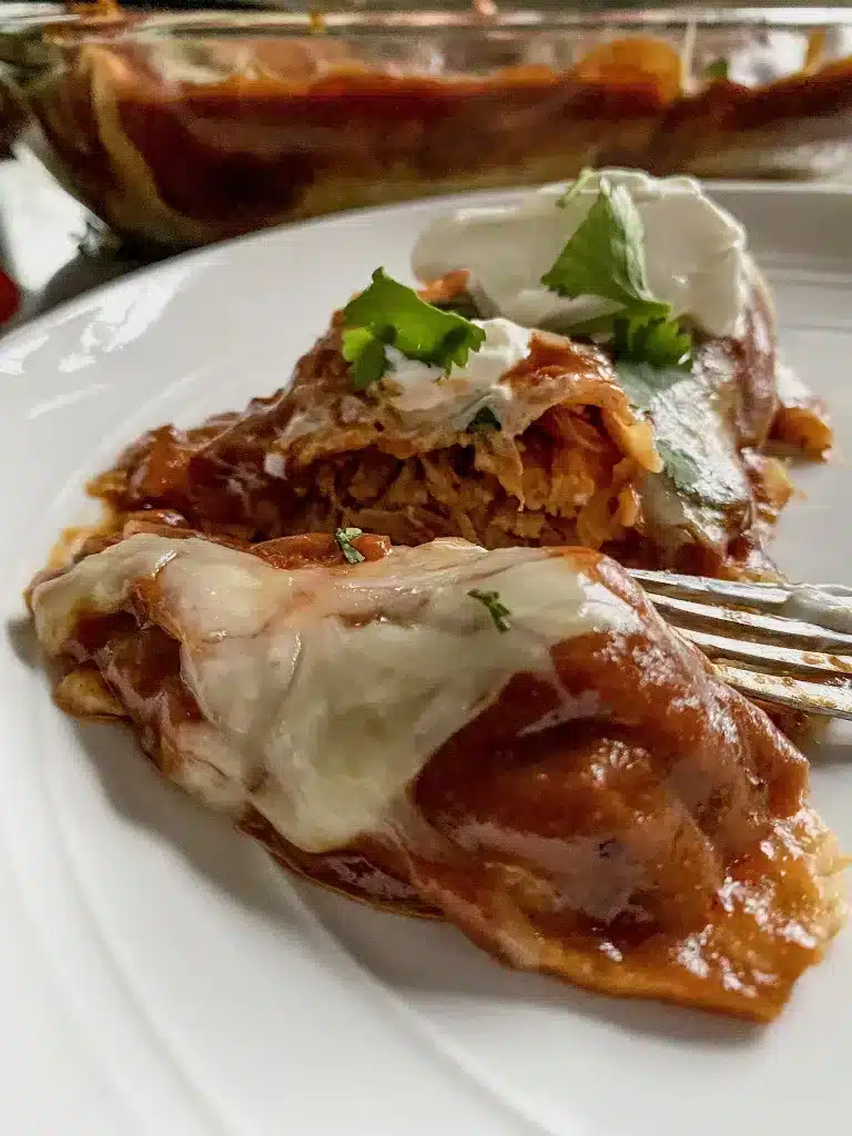a plate of red chicken enchiladas that are gluten free with cheese melted on top.