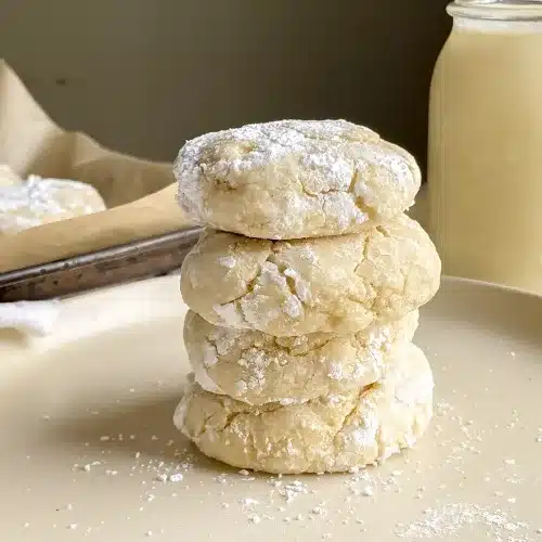 close up view of stack of gf gooey butter cookies on a plate with a cup of milk in background.