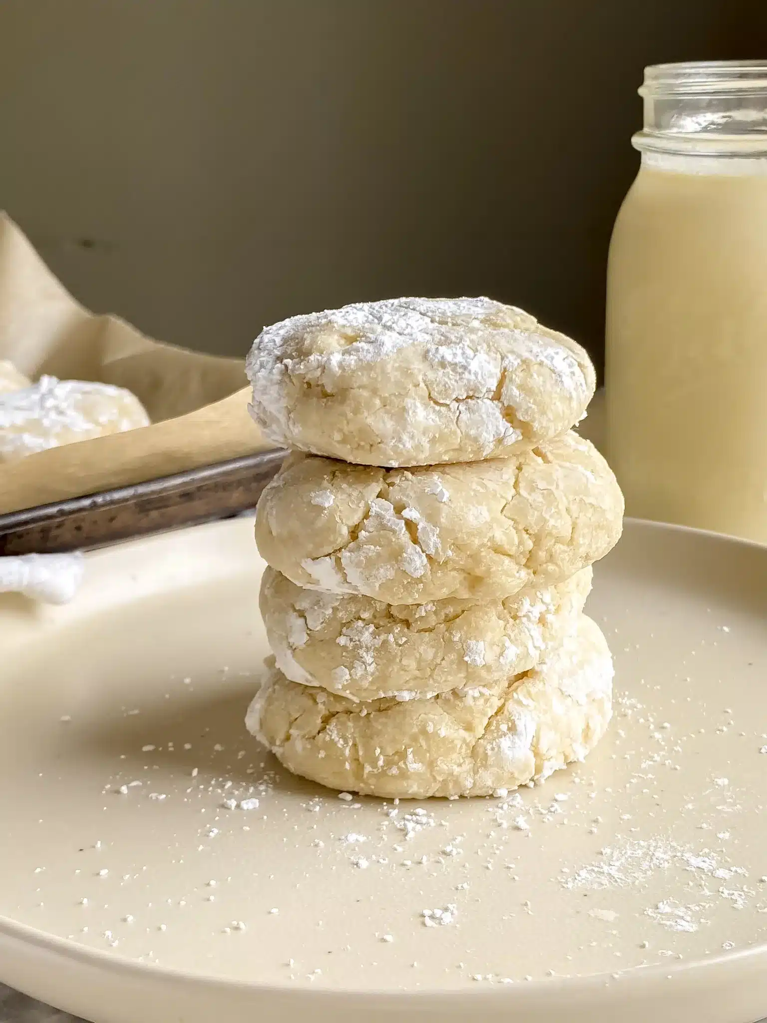 close up view of stack of gf gooey butter cookies on a plate with a cup of milk in background.