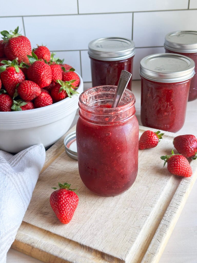 jars of homemade canned strawberry jam on counter top with fresh strawberries near by