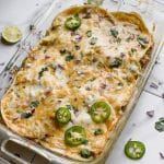 a glass 9 x 13 casserole pan with a batch of gf green enchilada chicken casserole on a counter with green chiles near by