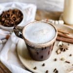 a hot chai tea latte that is better than starbucks in a brown mug on cream colored plate with spices around it