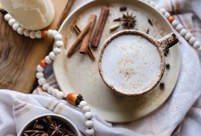 a chai tea latte sits on a plate filled with cinnimon sticks, star anise pods, whole cloves and all spice berries. With a bottle of milk near by