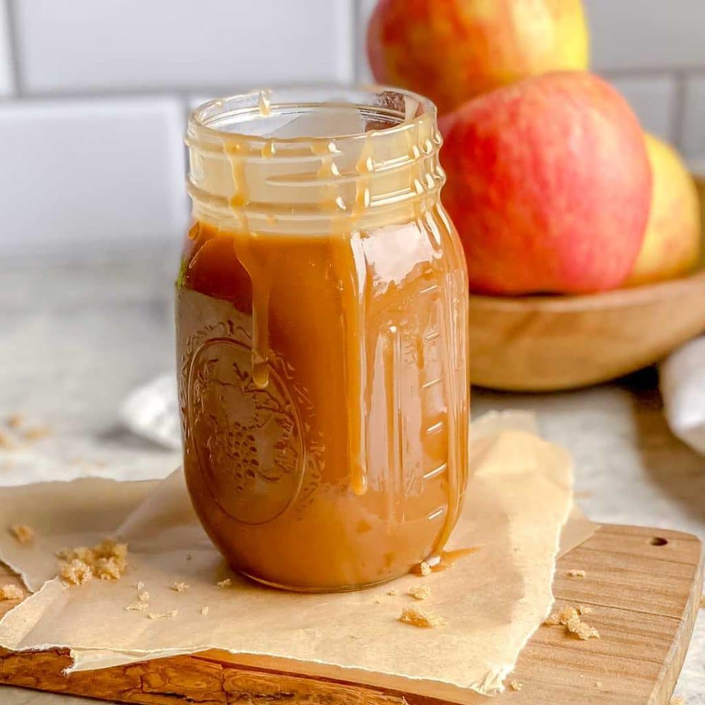 jar of homemade caramel sauce sitting on cutting board on counter top