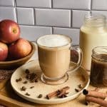 a mug of apple cider chai tea latte sits on a tan plate surrounded by warming spices included in the recipe