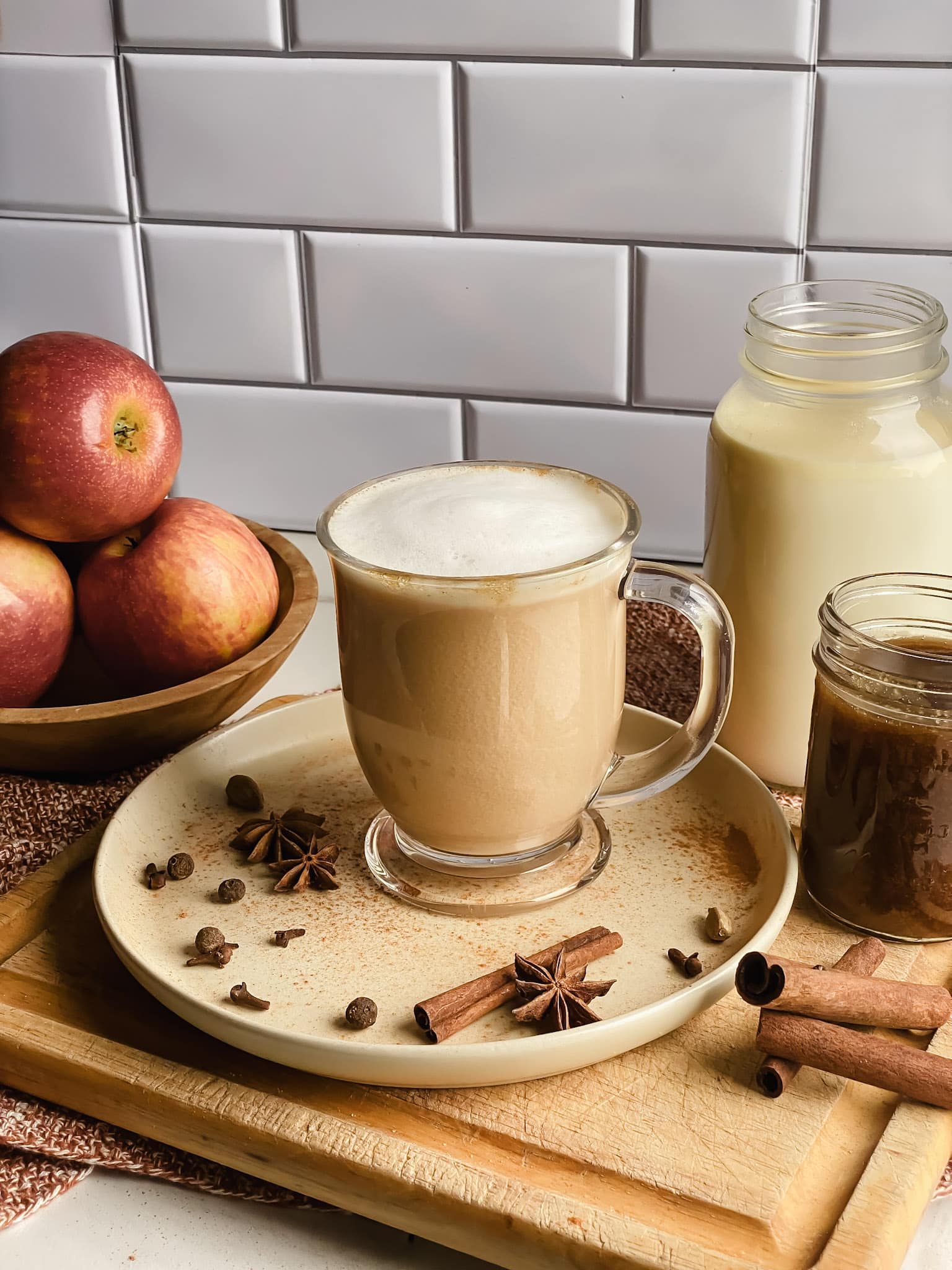 a mug of apple cider chai tea latte sits on a tan plate surrounded by warming spices included in the recipe