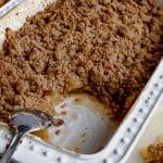 white baking dish with gluten free apple crisp without oats and a silver spoon removing a serving