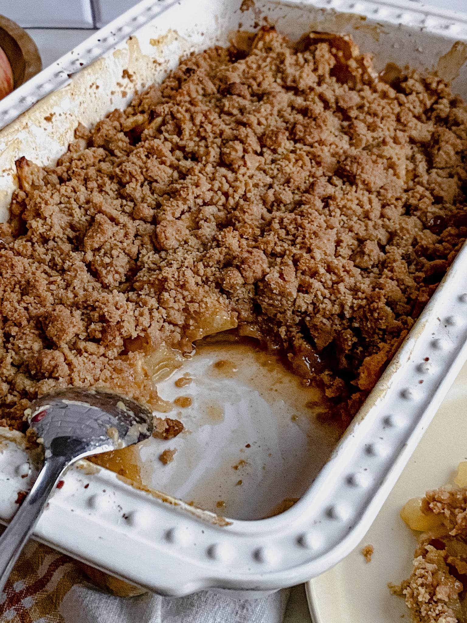 white baking dish with gluten free apple crisp without oats and a silver spoon removing a serving