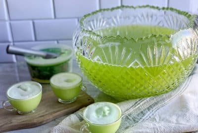 a bowl of green punch sits on counter with cups full of holiday punch and lime sherbet