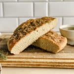 a sliced loaf of gluten free focaccia bread sits on a cutting board