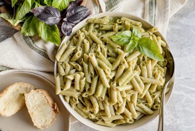 large bowl of gluten free pasta with dairy free creamy pesto pasta sauce with basil leaves