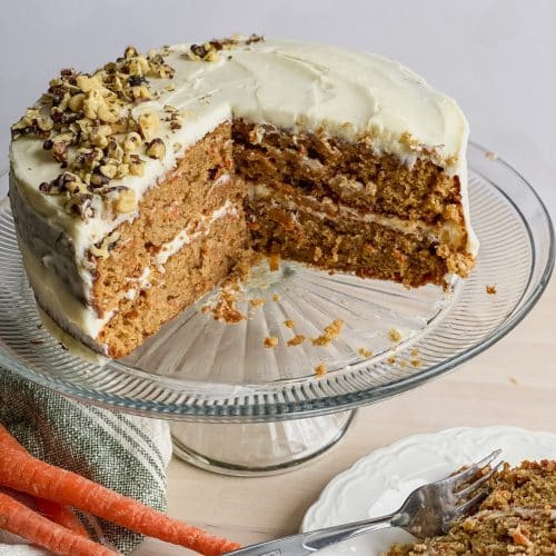 a double layer round gluten free carrot cake with cream cheese frosting sitting on a cake stand