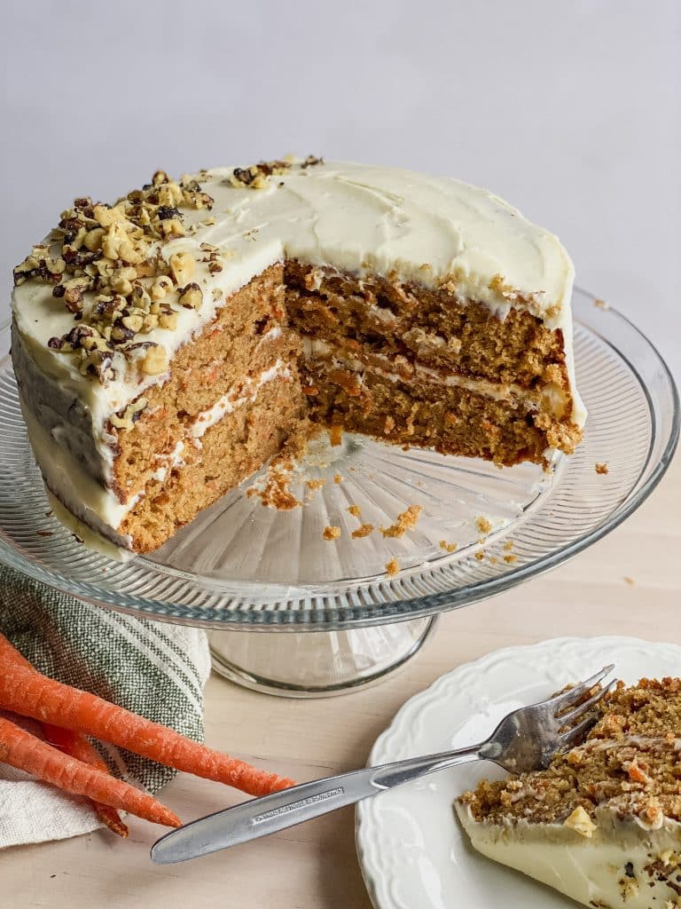 double layer round gf carrot cake with cream cheese frosting on a cake stand. walnuts sprinkled on the top