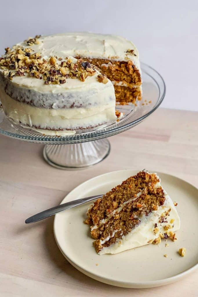 double layer round cake on a glass cake stand with a white plate and a slice on it