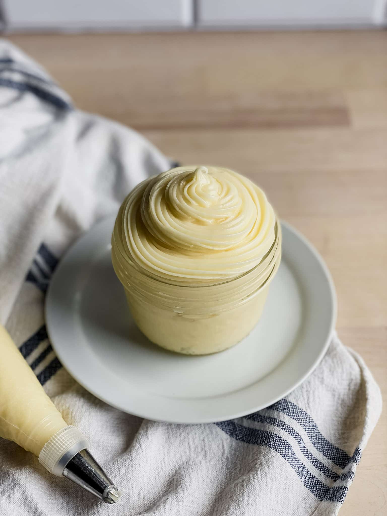 a cup of cream cheese icing on a white plate with a tea towel under it
