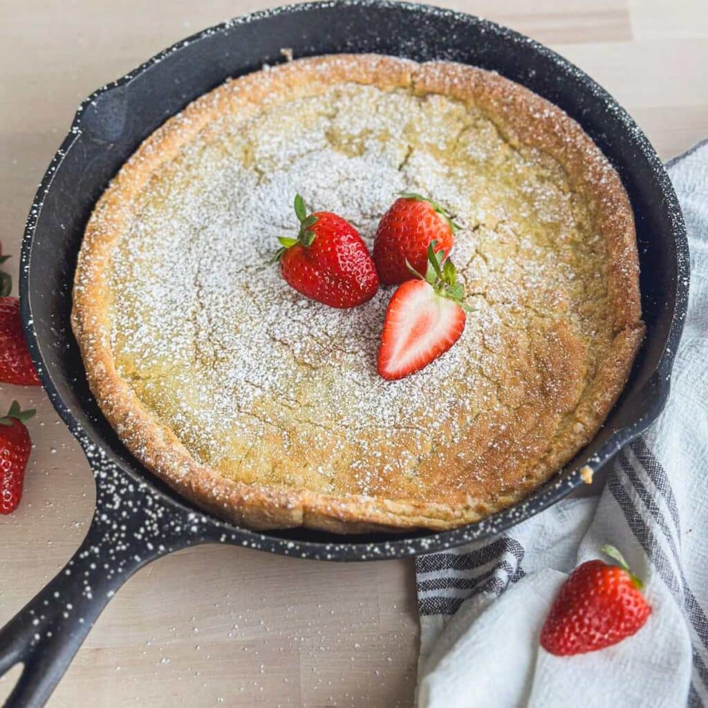 homemade easy oven pancake gluten free in a cast iron skillet with powdered sugar and strawberries
