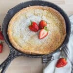 homemade easy oven pancake gluten free in a cast iron skillet with powdered sugar and strawberries