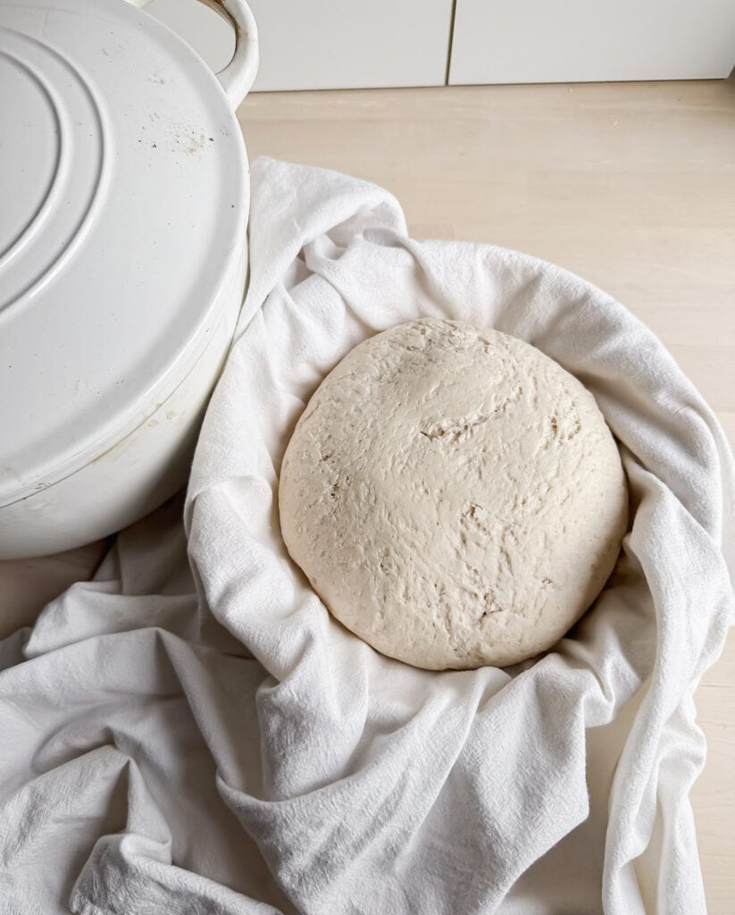 proofed dough in a banneton basket near a white Dutch oven