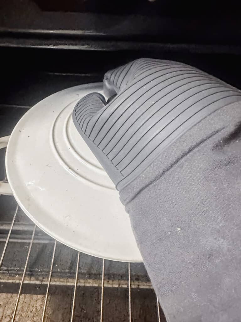 grey heat glove taking off the lid of the white Dutch oven