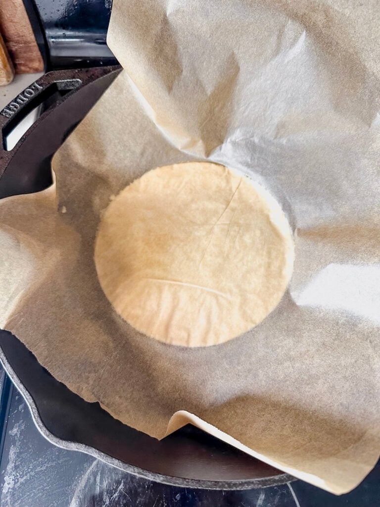 hot cast iron skillet with tortilla starting to cook with parchment paper still attached