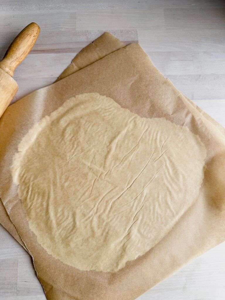 two pieces of parchment paper with gluten free tortilla dough pressed and rolled in between them