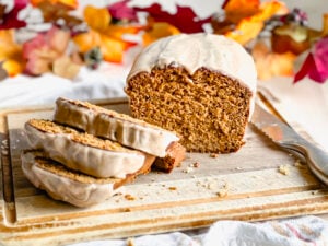 loaf of gluten free pumpkin bread on wooden cutting board with bread knife near by