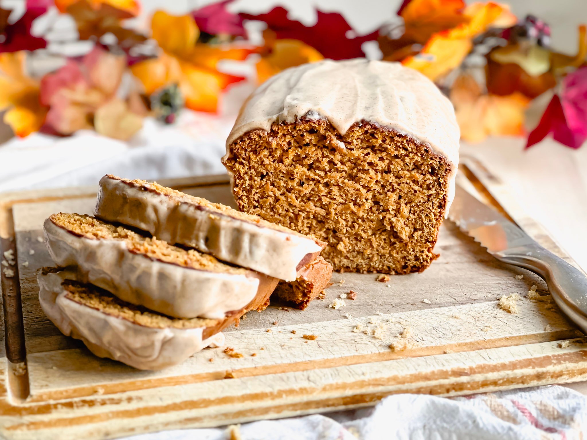 loaf of gluten free pumpkin bread on wooden cutting board with bread knife near by
