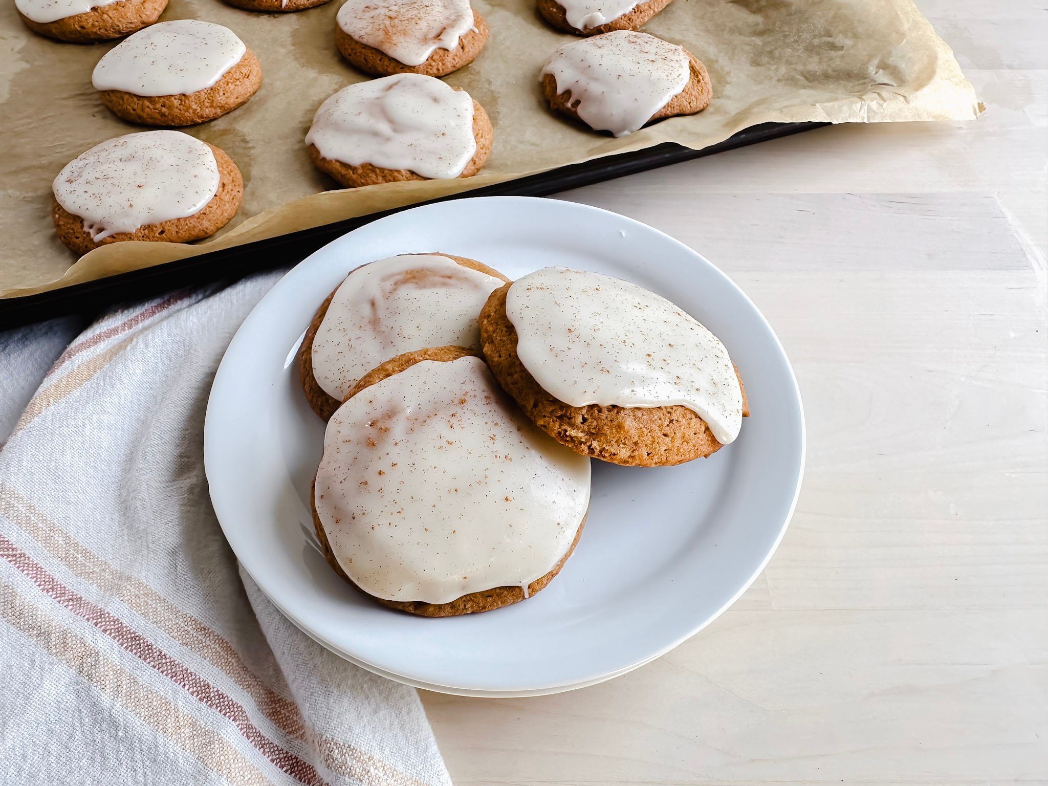 gluten free pumpkin cookies on a white plate with some on a baking sheet behind it